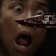 This image from The Walking Dead's final season depicts a bloody blade in the foreground, and a person's terrified face in the background.